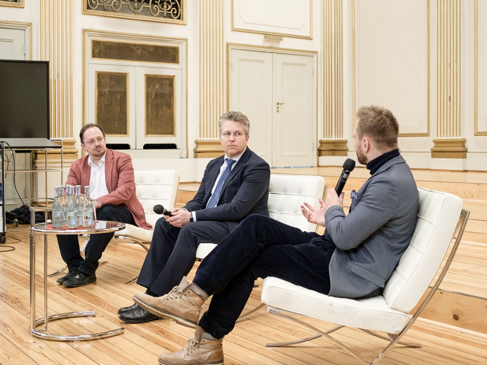 Drei Männer sitzen mit Mikrofonen auf einer Bühne und diskutieren in einem Podiumsgespräch.