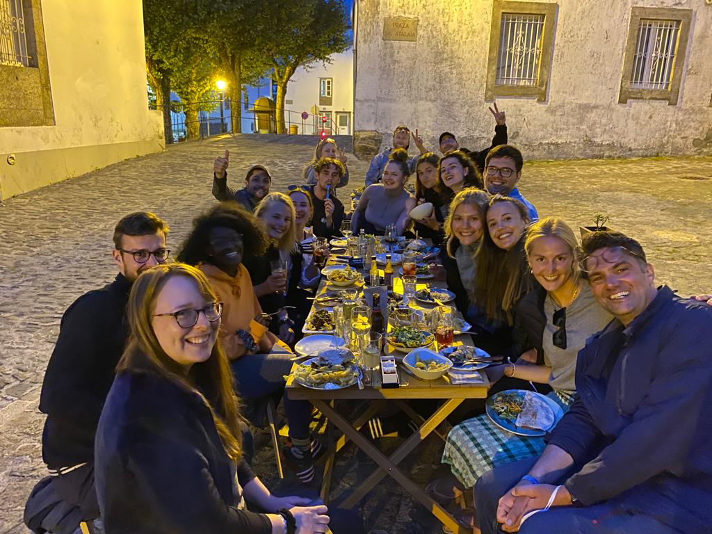 Gruppe von Menschen sitzt an einem langen Tisch im Freien und isst gemeinsam bei Abendstimmung.