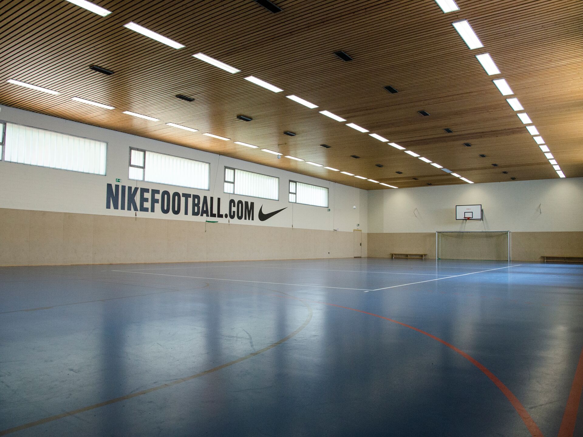 Leere Sporthalle mit blauen Bodenmarkierungen, Basketballkorb, Torwand und großem Nike-Wandlogo.