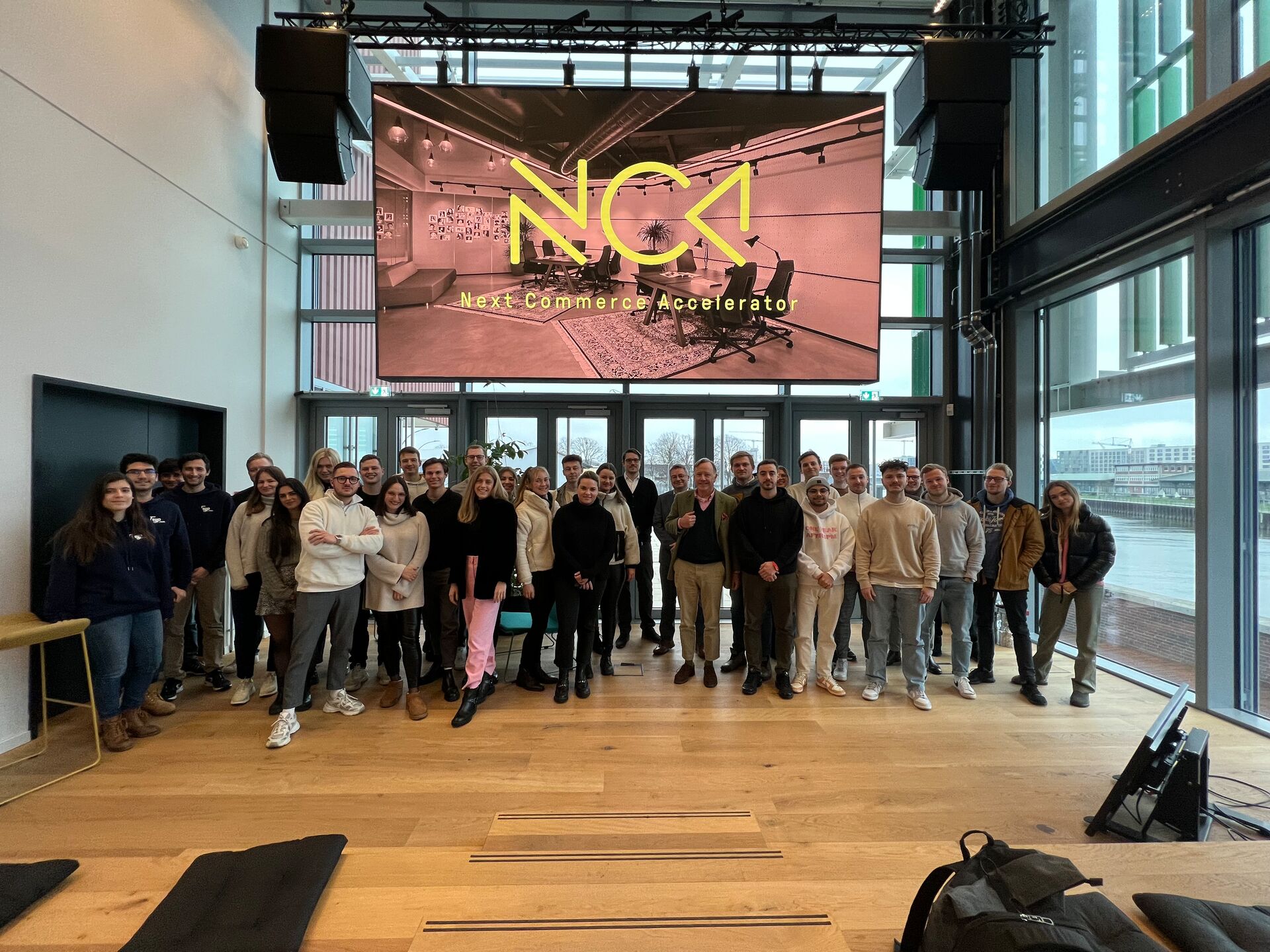 Gruppe von Menschen posiert vor einer Leinwand mit der Aufschrift NCA Next Commerce Accelerator.
