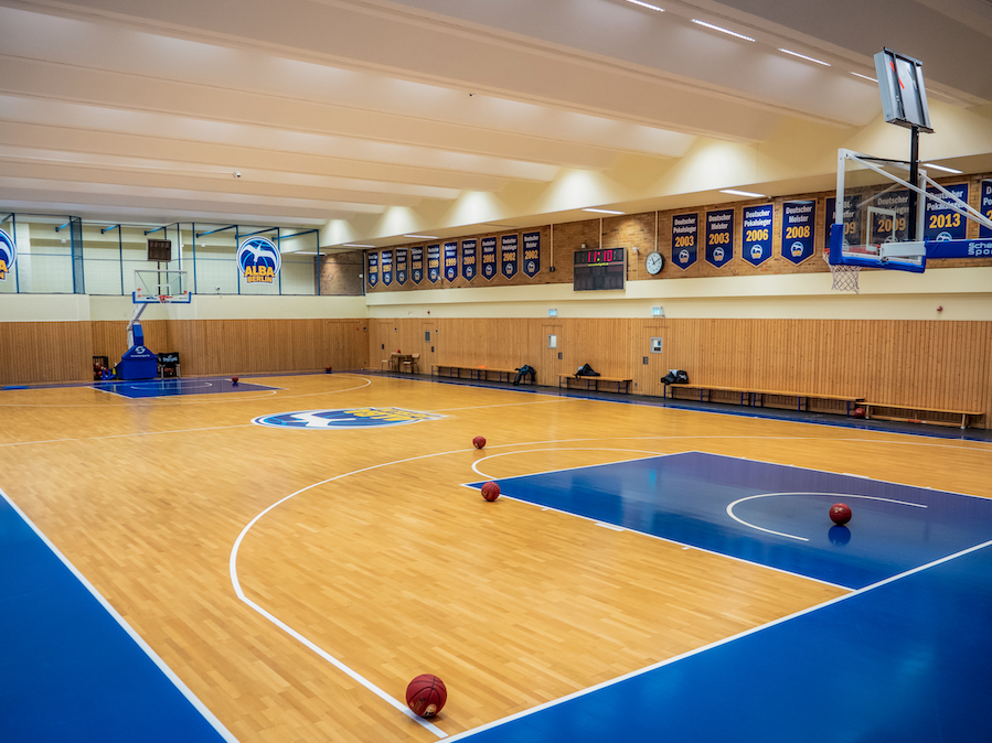 Leere Basketballhalle mit Holzboden, Körben, Bannern an der Wand und verstreuten Basketbällen.