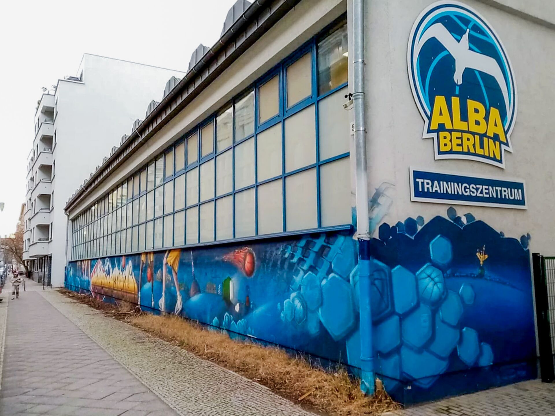 Gebäude mit großem ALBA Berlin Logo und der Aufschrift Trainingszentrum, bemalt mit buntem Basketball-Graffiti.