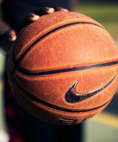 Hand hält einen Basketball mit sichtbarem Markenlogo im Vordergrund.