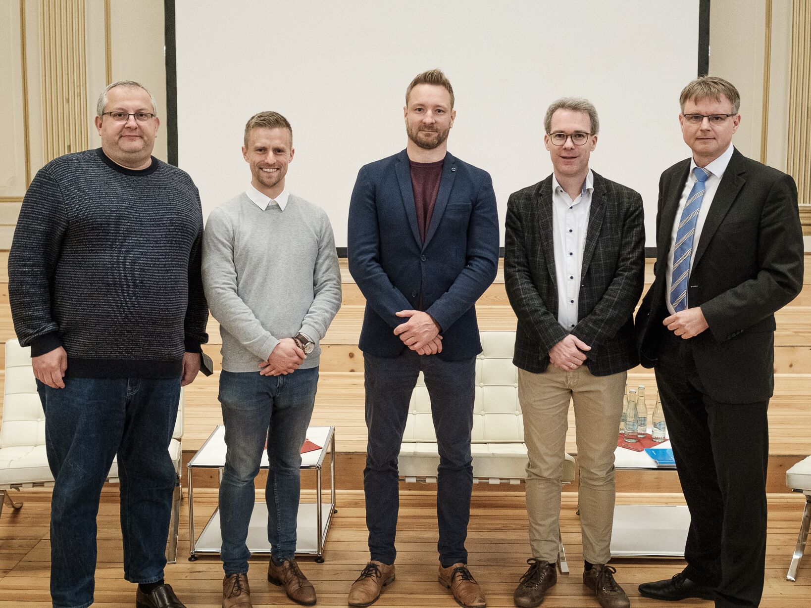 Fünf Männer stehen nebeneinander auf einer Bühne und posieren für ein Gruppenfoto.
