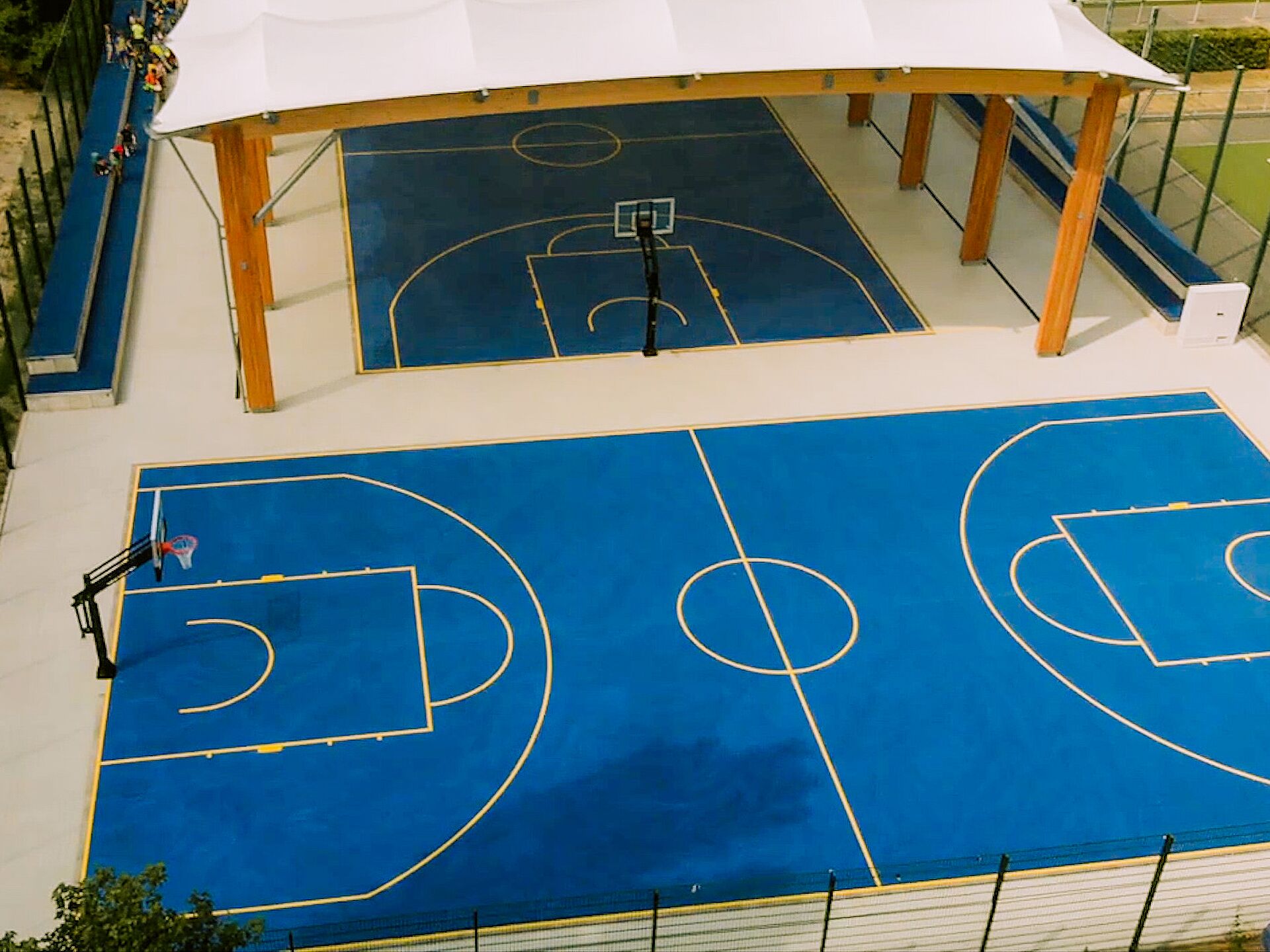 Überdachte blaue Basketballfelder im Freien mit Körben und Tribünen.