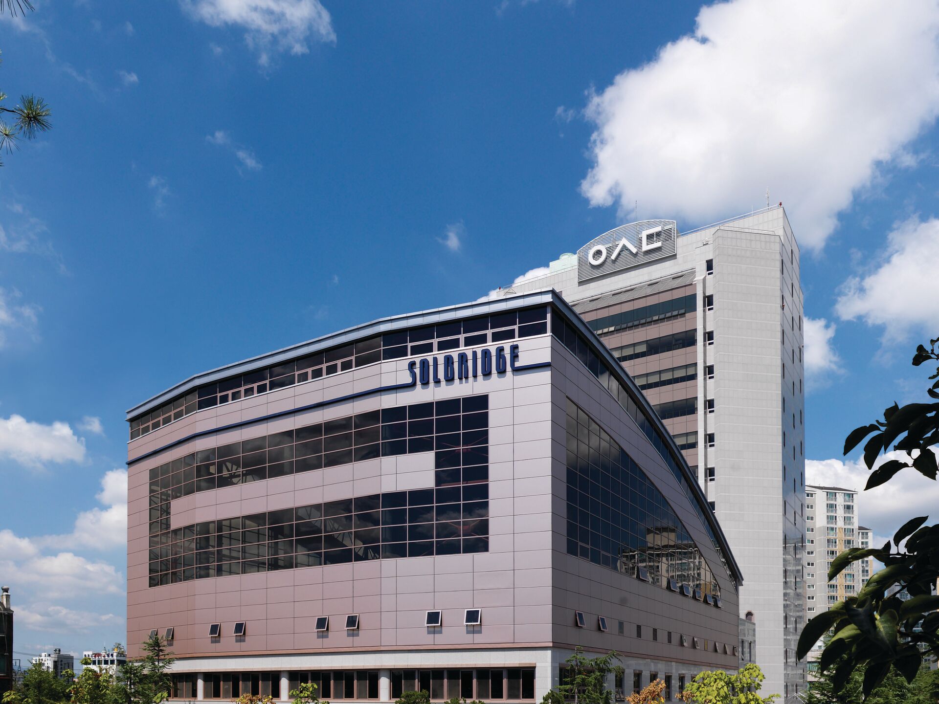 Modernes Universitätsgebäude mit großer Glasfassade und der Aufschrift SolBridge vor blauem Himmel.