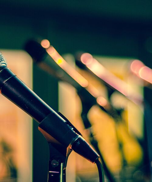 Nahaufnahme mehrerer Mikrofone auf Ständern, unscharf in einer Reihe hintereinander angeordnet.