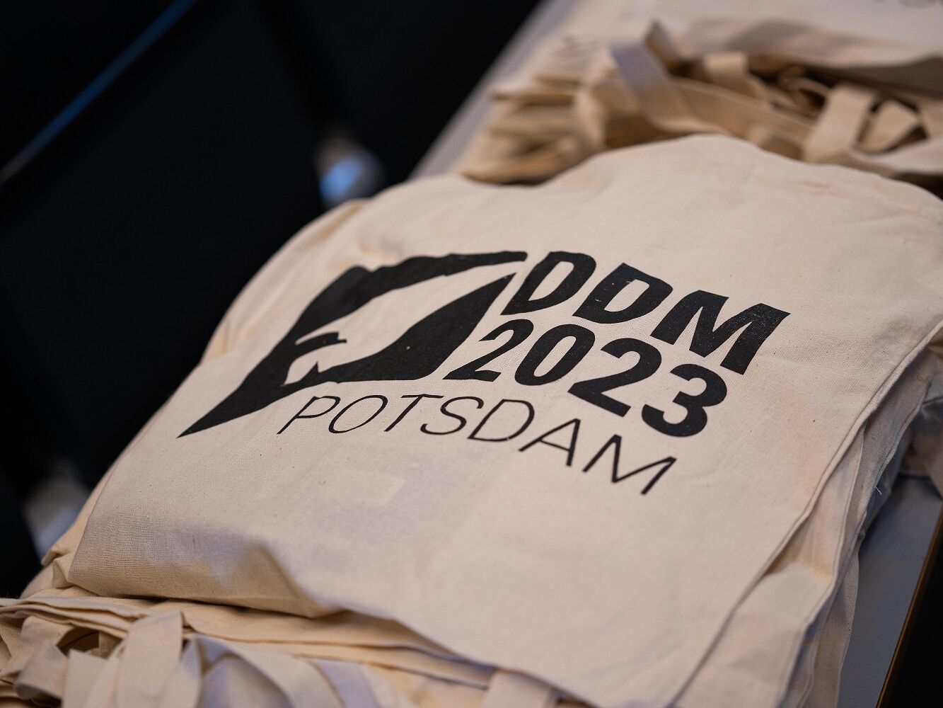Beige Stofftasche mit schwarzem Aufdruck „DDM 2023 POTSDAM“ und stilisiertem Logo eines Vogels.
