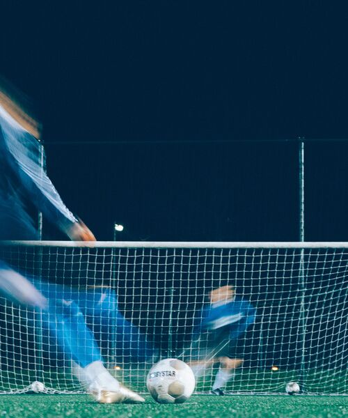Fußballspieler schießt bei Nacht ein Tor, der Ball liegt vor dem Netz.